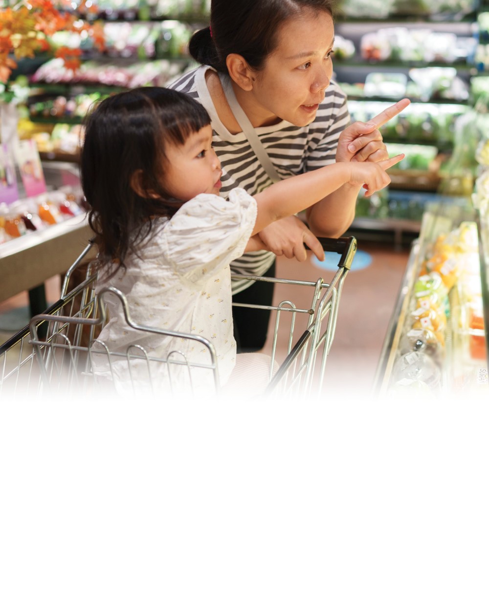 A mother and child point toward produce at a grocery store.