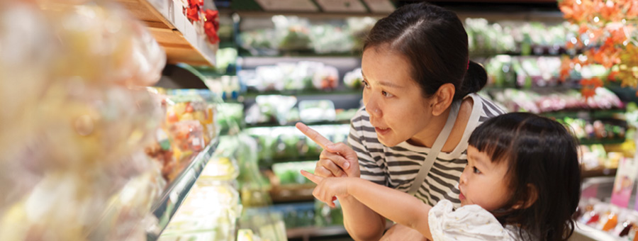 A mother and child point toward produce at a grocery store.