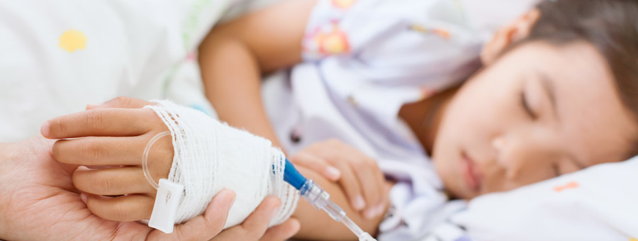 Child in hospital bed, caregiver holding hand.