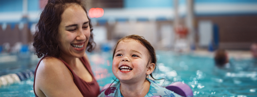 Woman helps child swim in pool.
