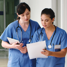 Two nurses discussing a file in the hallway.
