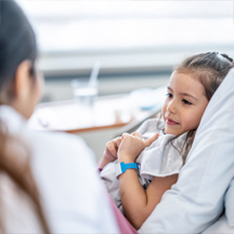 Girl in hospital bed looks at doctor.
